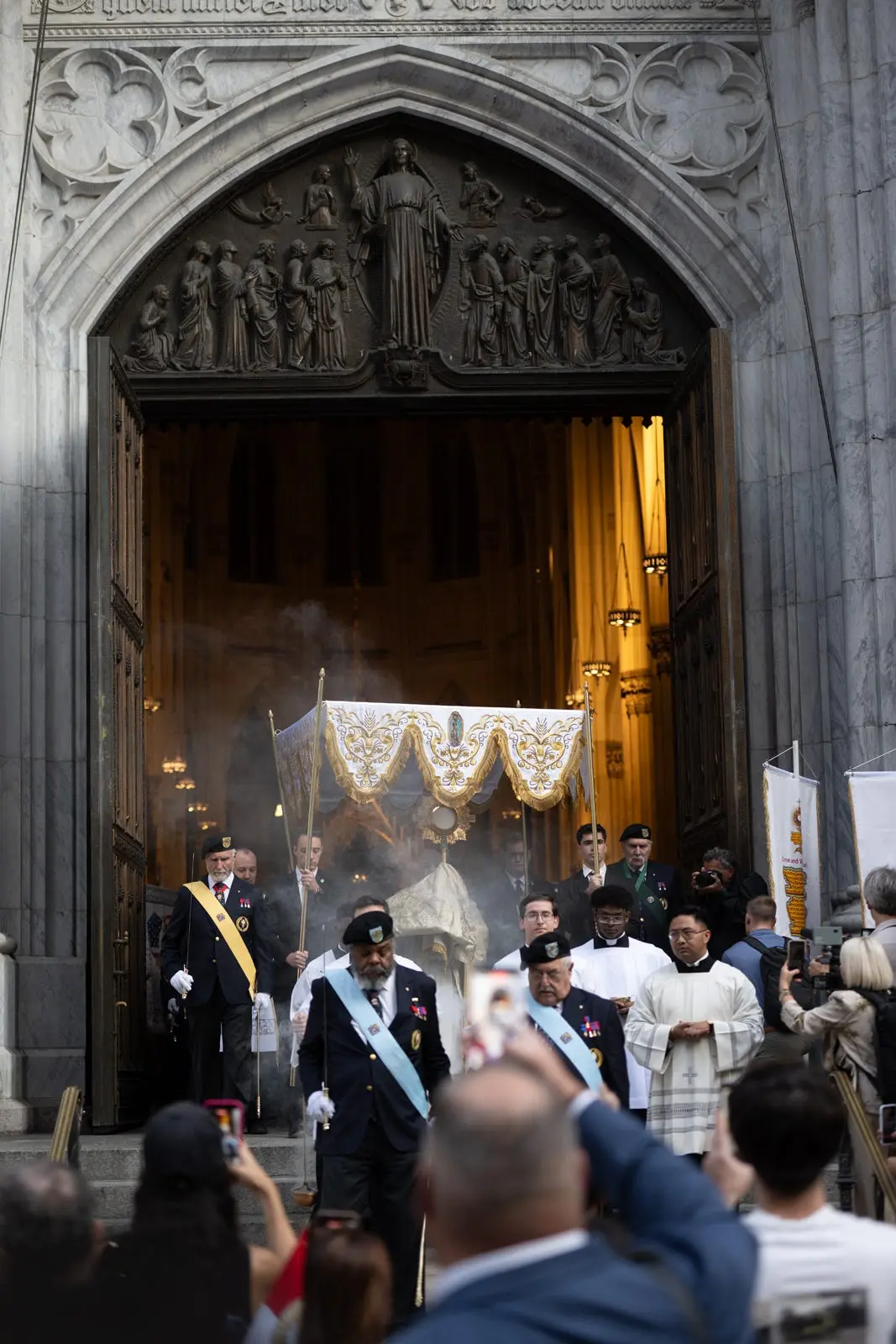 Beneath the figure of Christ above the cathedral doors, the Blessed Sacrament emerges through incense into the afternoon. The invitation is going out into the streets. | Credit: Jeffrey Bruno